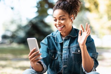 Akıllı Telefonlu Siyah Kadın Park 'ta oturmuş video görüşmesi yapıyor.