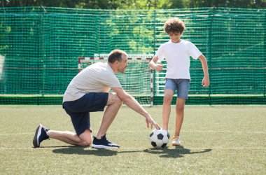 Yetişkin bir adam küçük bir çocuğa futbol oynamayı öğretiyor.