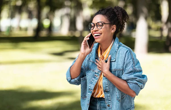 Glad afroamerikansk flicka pratar på mobiltelefon promenader i parken — Stockfoto