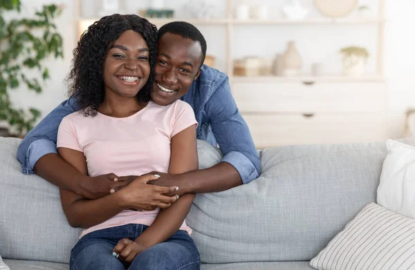 Веселий африканський чоловік обіймає усміхнену дружину ззаду — стокове фото