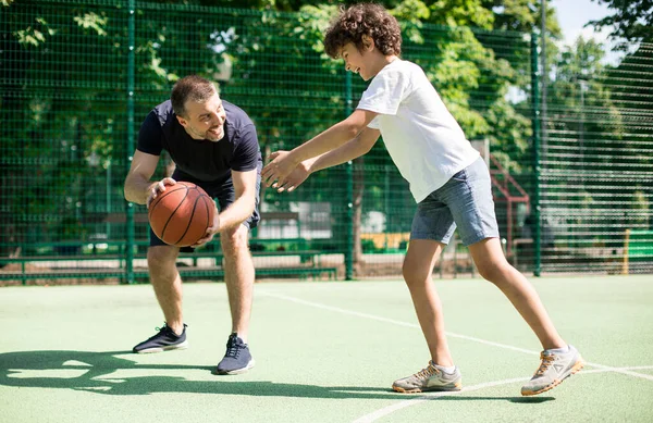 Χαρούμενος άντρας που μαθαίνει στο αγόρι πώς να παίζει μπάσκετ. — Φωτογραφία Αρχείου