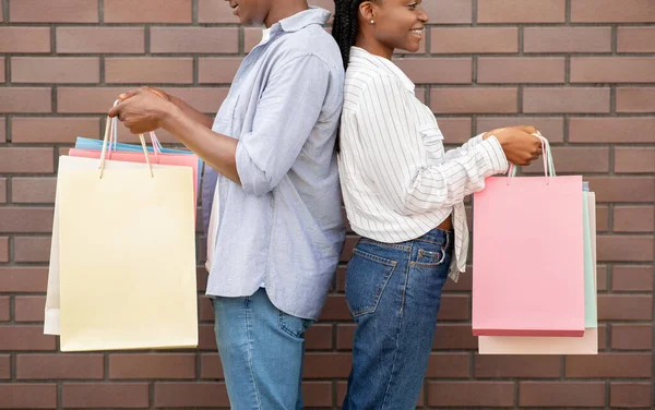 Compras e presentes. Africano casal americano em casual com sacos multicoloridos ficar para trás para o outro — Fotografia de Stock