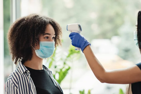 Africano americano mulher recebendo verificação de temperatura corporal no salão de beleza, vista lateral — Fotografia de Stock