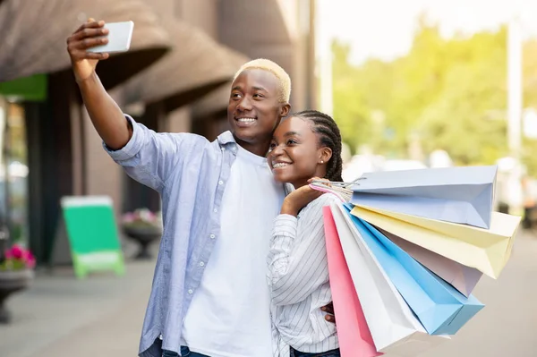 Foto van een gelukkig stel. Vrolijk Afrikaans amerikaanse man maakt selfie, meisje met tassen knuffels jongen — Stockfoto