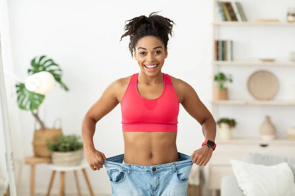 African Woman After Slimming Pokazuje stare spodnie oversize stojące w pomieszczeniach — Zdjęcie stockowe