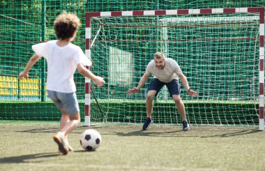 Küçük çocuk futbol oynuyor, topa vuruyor.