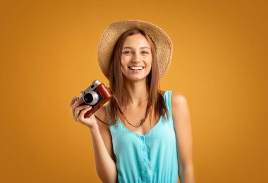 Gülümseyen kadın fotoğrafçı kamerayla sarıya poz veriyor.