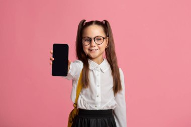 Teknoloji ve okul. Gözlüklü, üniformalı, telefonunu gösteren küçük çocuk.