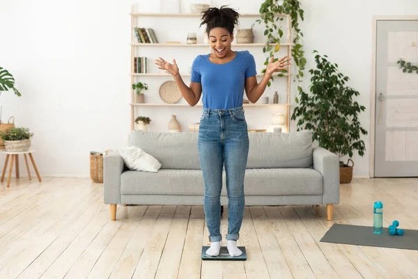 Excited Slim Black Girl Standing On Weight-Scales At Home, Full-Length