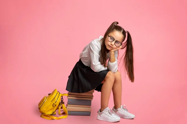Problemas en la educación escolar. Triste colegiala en gafas con mochila se sienta en un montón de libros — Foto de Stock