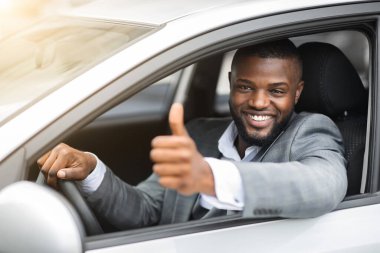 Mutlu siyah işadamı araba camından bakıyor, başparmağını gösteriyor.