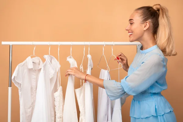 Ung kvinna väljer kläder står nära rack — Stockfoto