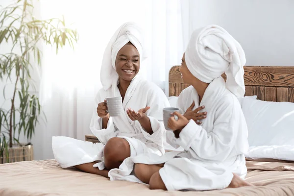 Meninas felizes em roupões de banho sentado na cama e beber café — Fotografia de Stock