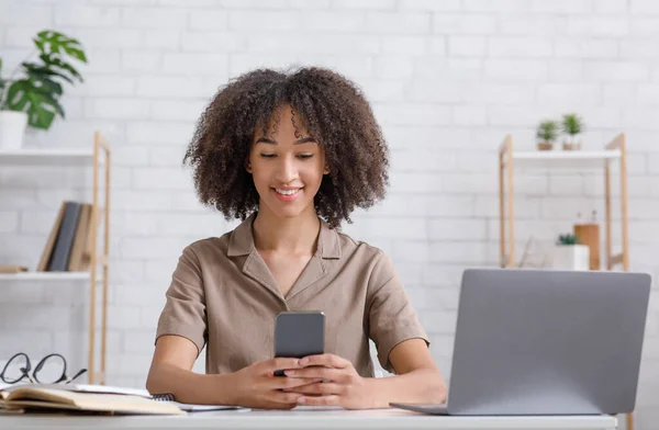 Dispositivi per studiare a casa durante la pandemia. Sorridente ragazza africana americana guardando smartphone — Foto Stock