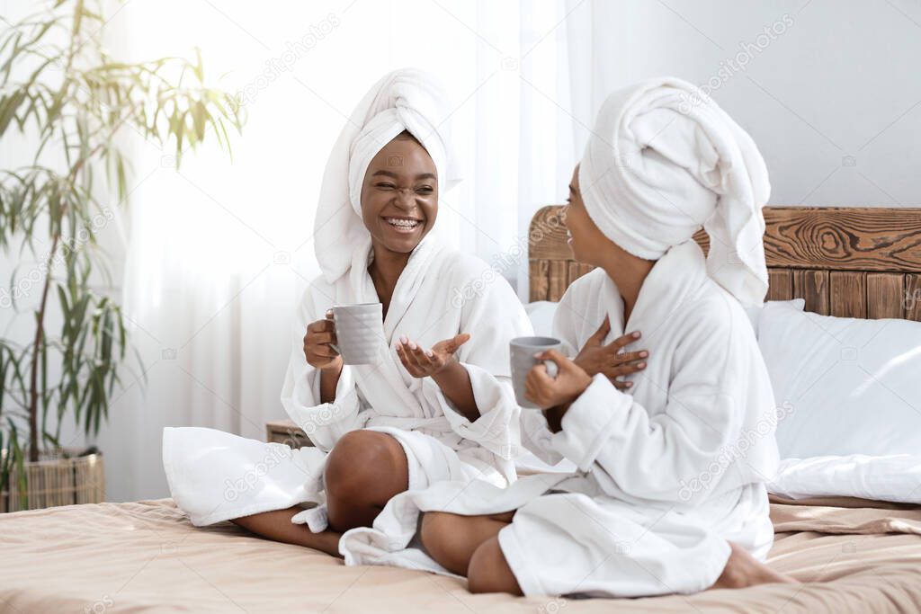 Happy girls in bathrobes sitting on bed and drinking coffee
