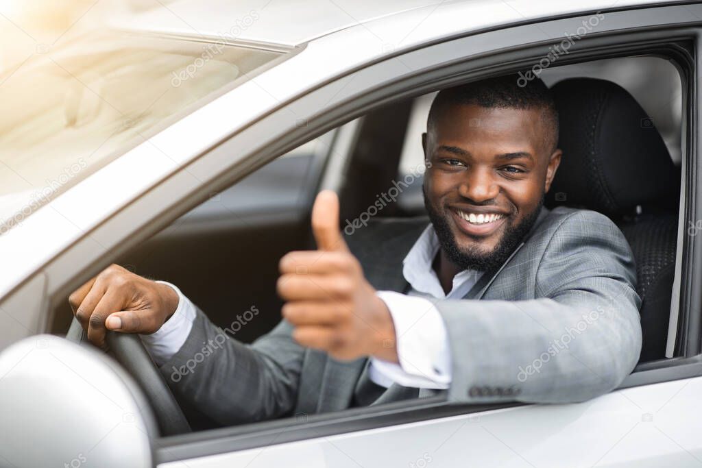 Happy black businessman looking through car window, showing thumb up