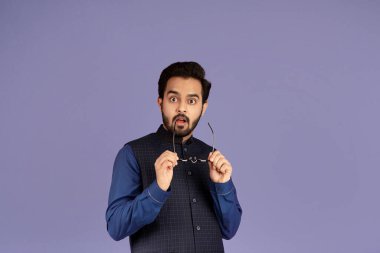 Yakışıklı Hintli adam gözlüğünü çıkarıyor ve menekşe arka planda şaşırarak ağzını açıyor.