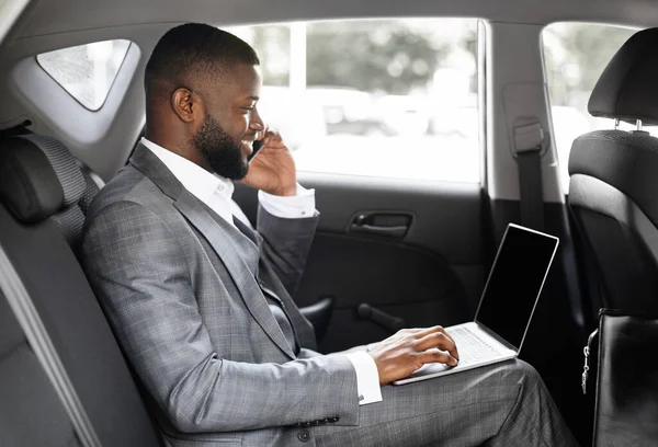 젊은 흑인 사업가가 차에서 휴대 전화와 노트북을 사용하는 모습 — 스톡 사진