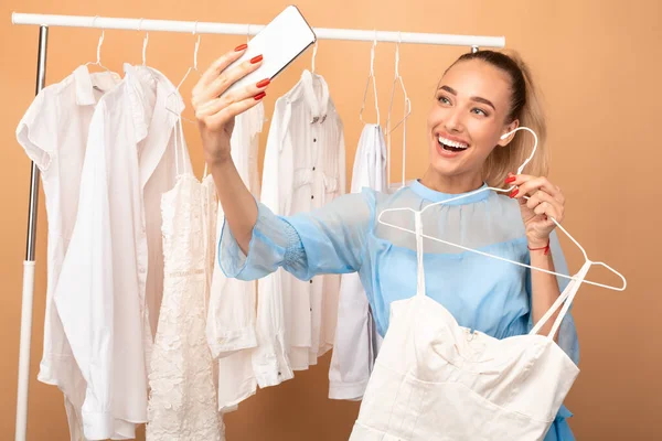 Šťastná žena se selfie stojící v blízkosti stojanu s oblečením — Stock fotografie