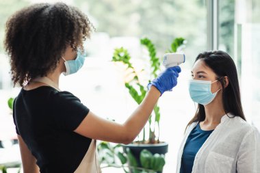 Güzellik salonundaki müşterinin vücut ısısını kontrol eden yönetici, yan görünüm