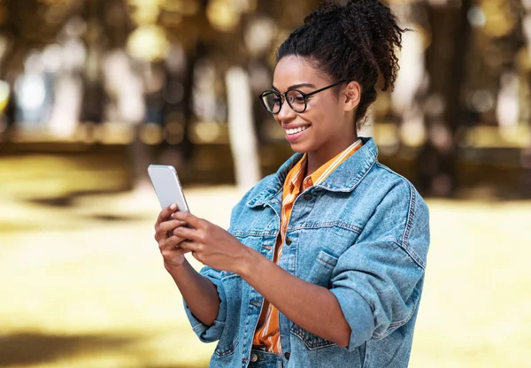Alegre africano millennial chica usando teléfono caminando en parque al aire libre —  Fotos de Stock