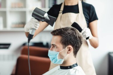 Koruyucu maskeli genç adam berber dükkanında saç stili yaptırıyor.