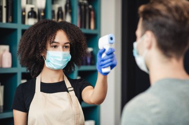 Berber dükkanında dokunulmaz termometreyle müşteri sıcaklığını tarayan kadın güzellik uzmanı.