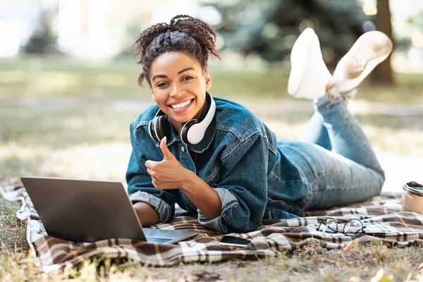 Nero ragazza utilizzando computer portatile gesturing pollice-up apprendimento in parco all'aperto — Foto Stock