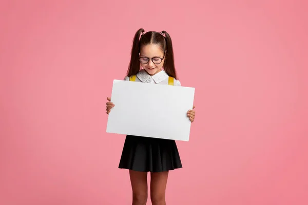 Scuola privata. Piccola bambina in occhiali e uniforme scolastica tiene tavolo con spazio vuoto — Foto Stock