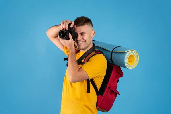 Szczęśliwy młody podróżnik z plecakiem i aparatem fotograficznym gotowy do robienia zdjęć na niebieskim tle — Zdjęcie stockowe