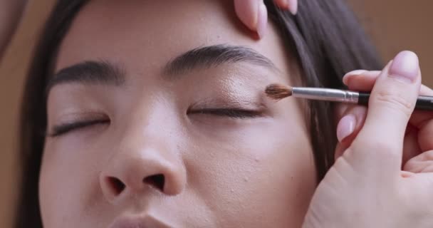 Visagist applying beige eyeshadows on asian girl eyes, close up — Stock Video