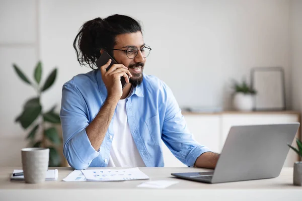 Komunikacja biznesowa. młody indyjski mężczyzna przedsiębiorca mówi na komórkę podczas pracy na laptopie — Zdjęcie stockowe