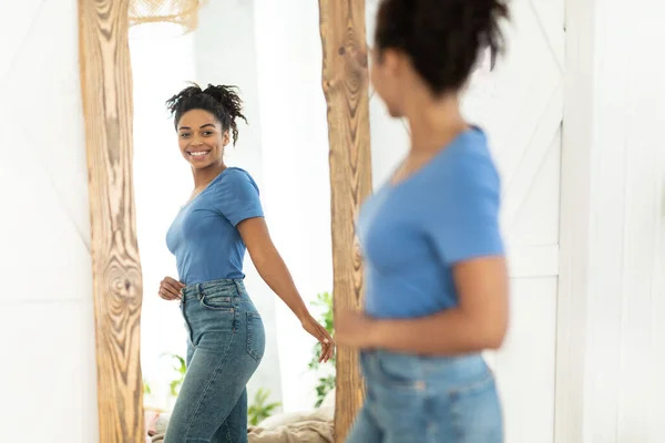 Chica afroamericana alegre después de adelgazar mirando en el espejo interior —  Fotos de Stock