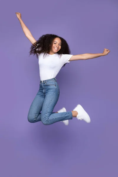 Mulher afro-americana feliz pulando posando no meio do ar, fundo roxo — Fotografia de Stock