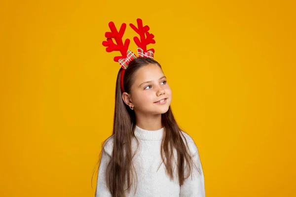 Criança à espera do Pai Natal. Menina bonita com chifres em suéter olha para o espaço vazio — Fotografia de Stock