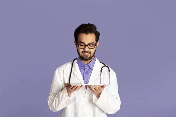 사이버 약. 긍정적 인 인도의 의사가 태블릿 컴퓨터, 라일락 배경을 통해 환자와 온라인으로 대화하는 모습 — 스톡 사진