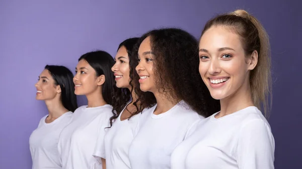 Gelukkig multi-etnische vrouwen staan in rij poseren over paarse achtergrond, — Stockfoto