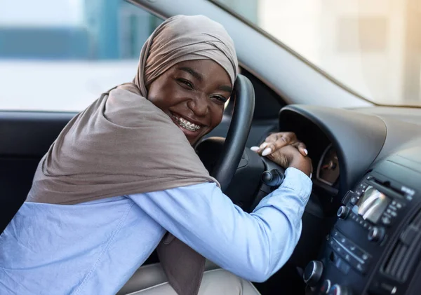 Primer coche. feliz negro musulmán mujer en hijab abrazando volante — Foto de Stock