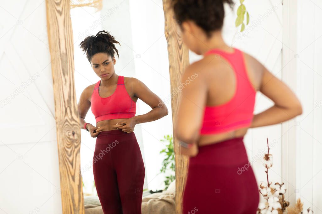 Unhappy African Woman Touching Fat Belly Standing Near Mirror Indoor