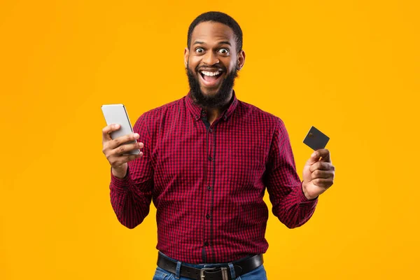 Opgewonden zwarte man met creditcard en mobiele telefoon in de studio — Stockfoto
