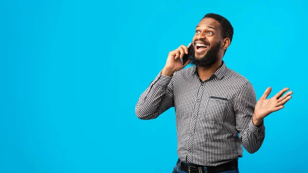 Hombre negro sonriente hablando por teléfono, pared azul — Foto de Stock