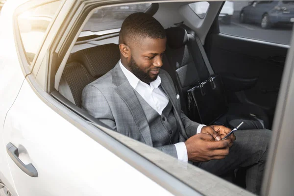 Feliz hombre de negocios africano usando el teléfono móvil mientras está sentado en taxi —  Fotos de Stock