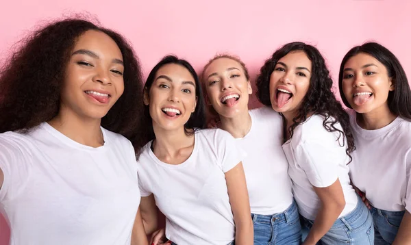 Multicultural senhoras fazendo grupo selfie mostrando línguas sobre fundo rosa — Fotografia de Stock