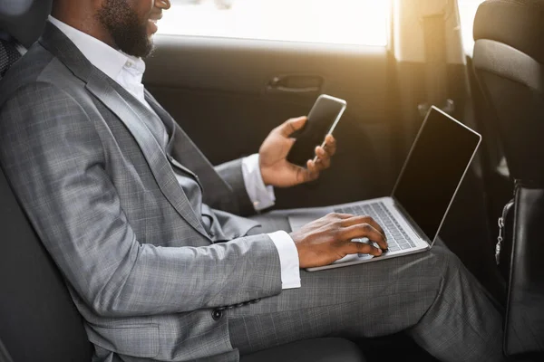Afrikanischer Geschäftsmann benutzt Smartphone und Laptop im Auto — Stockfoto