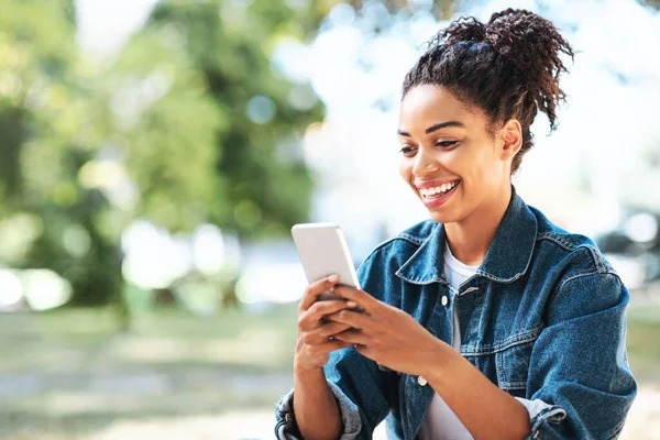 Happy Black Girl Korzystanie z aplikacji Telefon komórkowy siedzi na zewnątrz — Zdjęcie stockowe