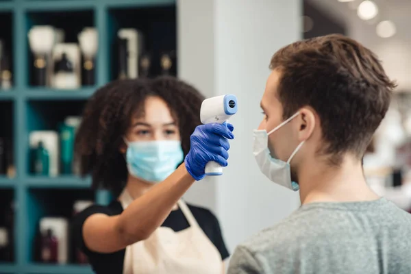 Cabeleireiro mulher medir a temperatura corporal do jovem cliente masculino na barbearia — Fotografia de Stock