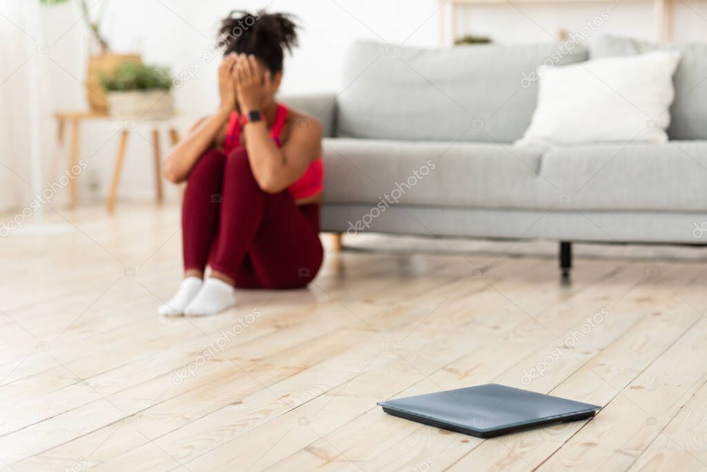 Desperate African Woman Crying Sitting Near Scales Gaining Weight Indoor