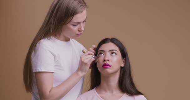 Maquillaje artista acabado glam buscar joven asiático mujer en salón, beige estudio fondo — Vídeos de Stock