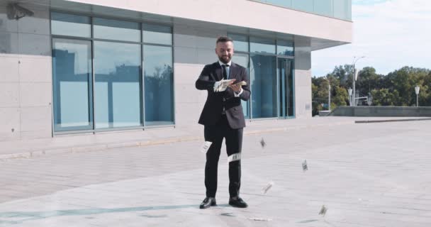 Успішний бізнесмен у костюмі кидає гроші, що стоять біля офісної будівлі — стокове відео