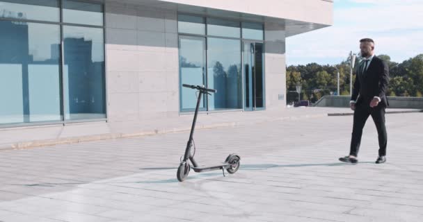 Affärsman i kostym kommer till elektrisk skoter och rider iväg — Stockvideo